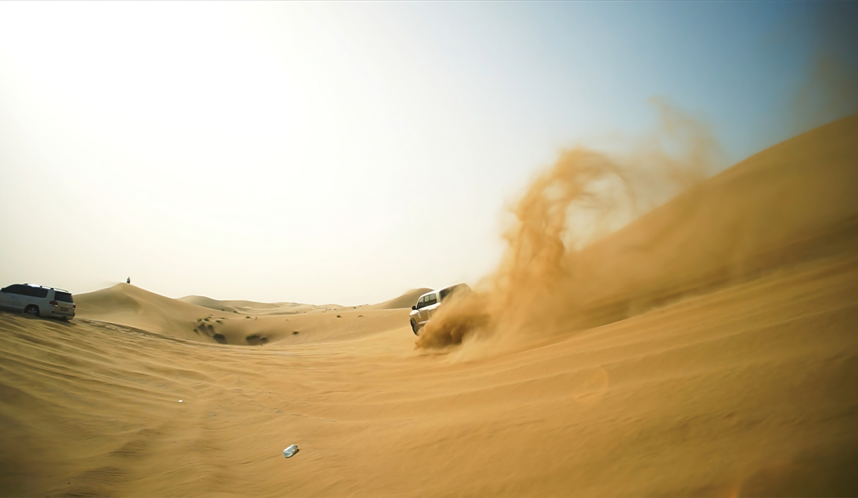 An SUV powers through the golden sand dunes during a desert safari in Dubai, kicking up a dramatic swirl of sand under the bright desert sky, symbolizing the adventure and excitement of dune bashing.