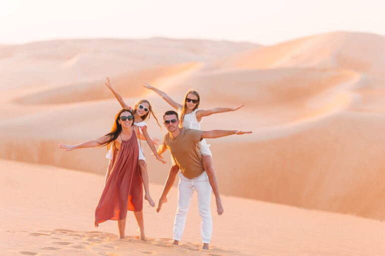 “Family posing playfully on desert dunes at sunset.”