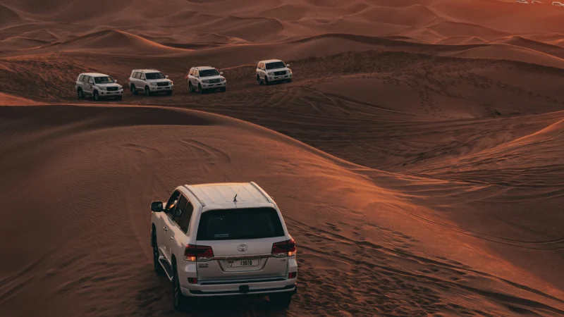 Evening desert safari Dubai with 4x4 Land Cruiser dune bashing across golden sand dunes at sunset