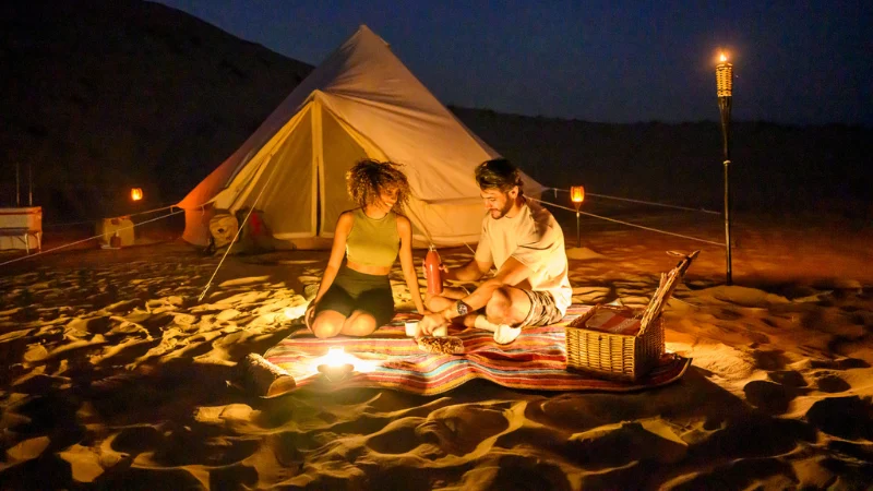 Dubai overnight desert safari camping with couple relaxing near tent under night sky in UAE desert